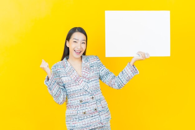 Portrait beautiful young asian woman with empty white billboard on color wall