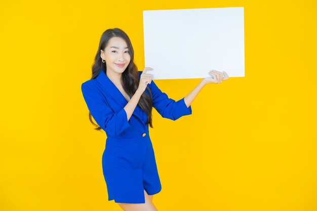 Free photo portrait beautiful young asian woman with empty white billboard on yellow