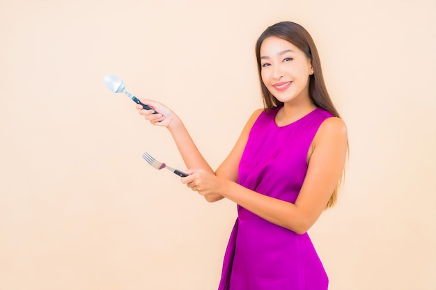 Portrait beautiful young asian woman with fork and spoon ready to eat on color background