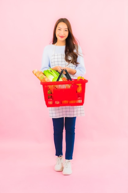 Free photo portrait beautiful young asian woman with fruit vegetable and grocery in basket on pink isolated wall