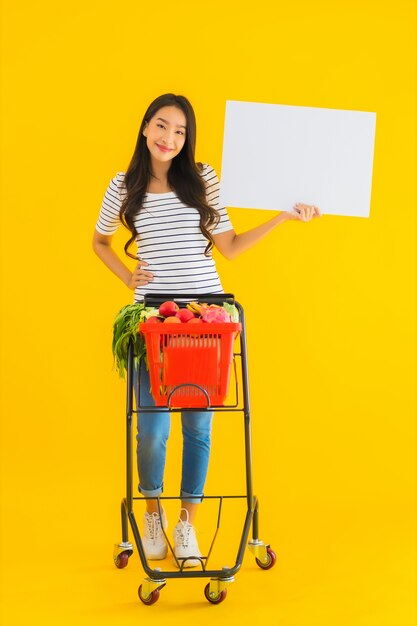 Portrait beautiful young asian woman with grocery basket cart and show white empty board