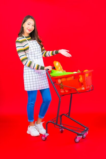 赤い孤立した壁にスーパーマーケットから食料品バスケットを持つ肖像画美しい若いアジアの女性