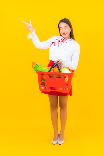 Portrait beautiful young asian woman with grocery basket from supermarket on yellow