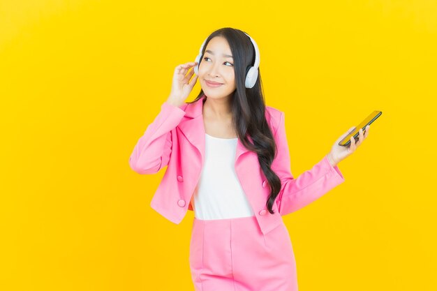 노란색 벽에 듣는 음악을위한 헤드폰 및 스마트 폰과 세로 아름다운 젊은 아시아 여자