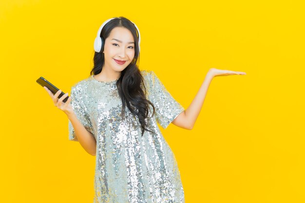 노란색에 듣는 음악에 대 한 헤드폰 및 스마트 폰 초상화 아름 다운 젊은 아시아 여자