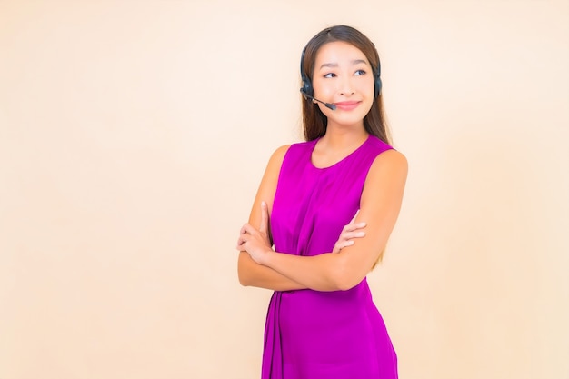 色の背景にコールセンターの顧客のためのヘッドセットを持つ肖像画の美しい若いアジアの女性