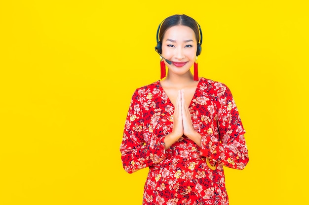 노란색 벽에 고객 콜 센터 관리를위한 헤드셋과 세로 아름다운 젊은 아시아 여자