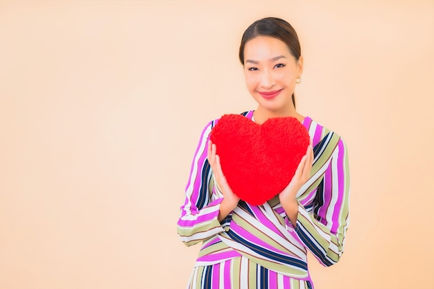 Bella giovane donna asiatica del ritratto con la forma del cuscino del cuore sul colore