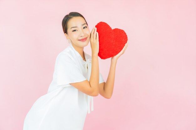 Portrait beautiful young asian woman with heart pillow shape on pink wall