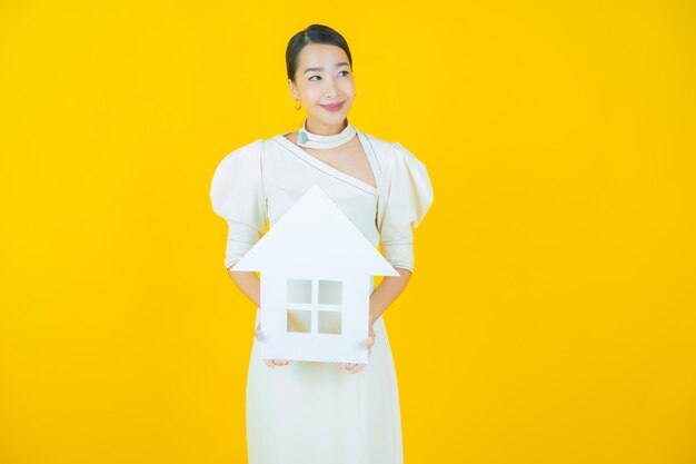 Женщина портрета красивая молодая азиатская с домом или домашним бумажным знаком на цветном фоне