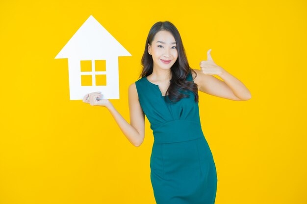 Portrait beautiful young asian woman with house or home paper sign on yellow