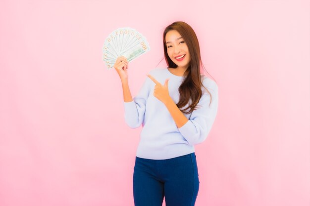 Женщина портрета красивая молодая азиатская с большим количеством наличных денег и денег на стене розового цвета