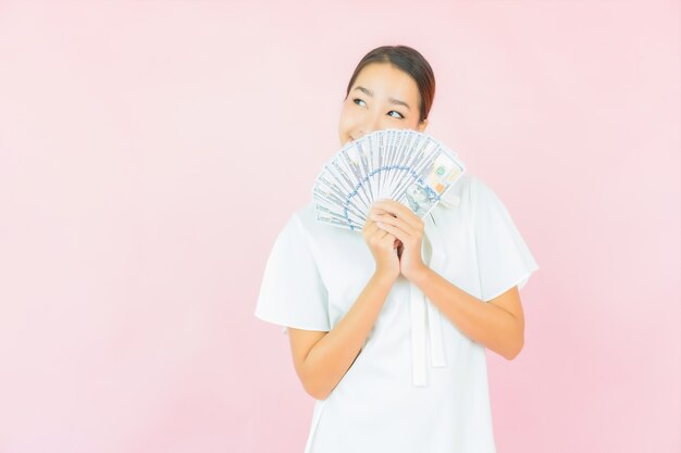 ピンク色の壁にたくさんの現金とお金を持つ肖像画の美しい若いアジアの女性