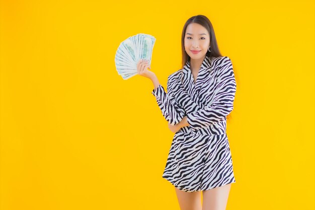Портрет красивая молодая азиатская женщина с большим количеством денег и денег на желтом