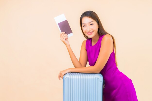 Портрет красивой молодой азиатской женщины с багажом и билетом на самолет на цветном фоне