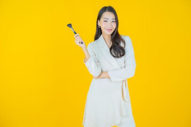 Женщина портрета красивая молодая азиатка с косметикой кисти на цветном фоне