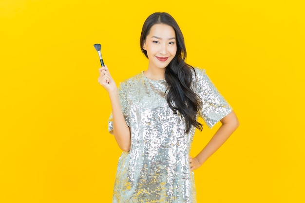 Portrait beautiful young asian woman with make up brush cosmetic on yellow