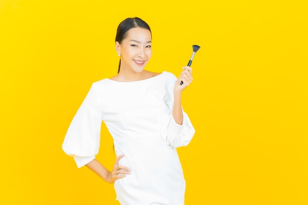 Portrait beautiful young asian woman with make up brush cosmetic on yellow