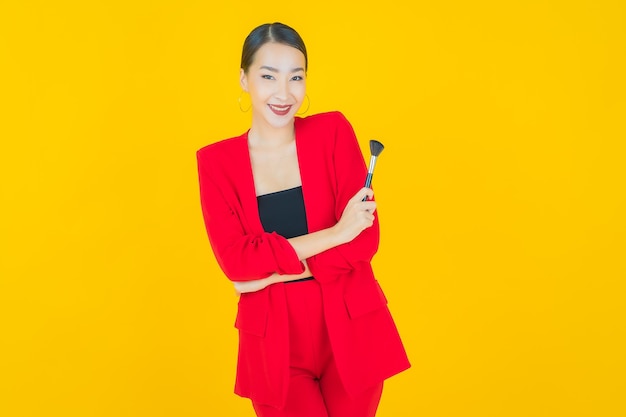 Portrait beautiful young asian woman with make up brush cosmetic on yellow