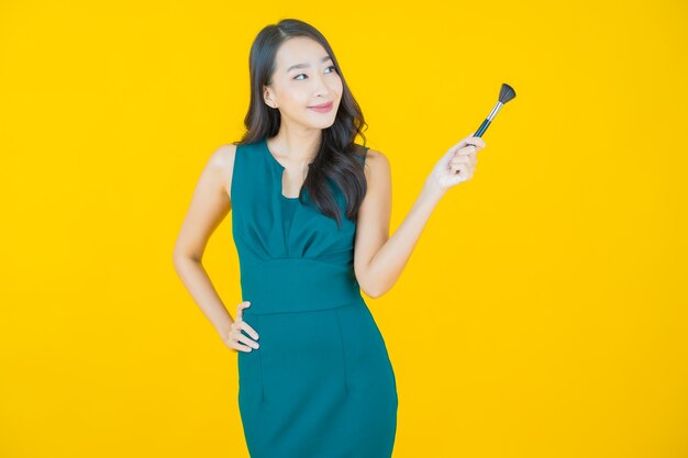 Женщина портрета красивая молодая азиатская с косметикой кисти на желтом