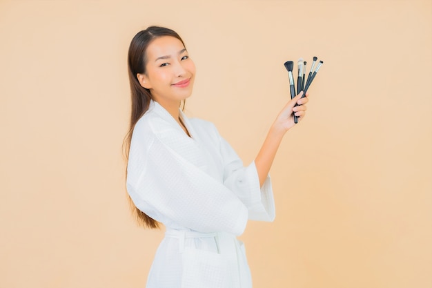 Portrait beautiful young asian woman with makeup brush on beige