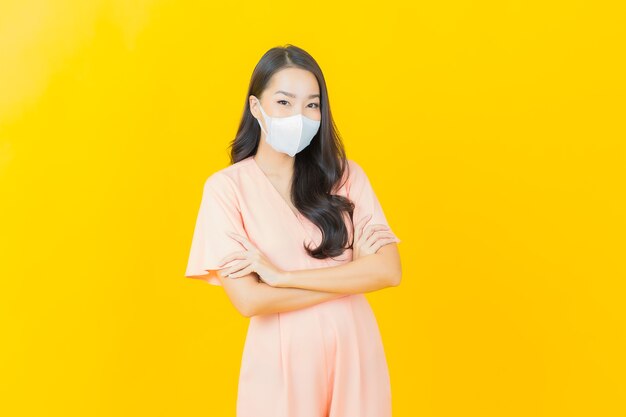 Портрет красивой молодой азиатской женщины с маской для защиты вируса covid19 на стене желтого цвета