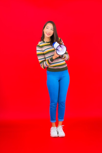 Free photo portrait beautiful young asian woman with megaphone for communication on red wall