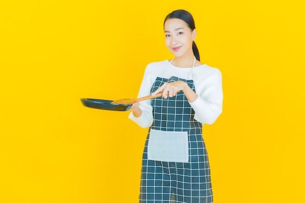 Free photo portrait beautiful young asian woman with pan and big spoon on yellow