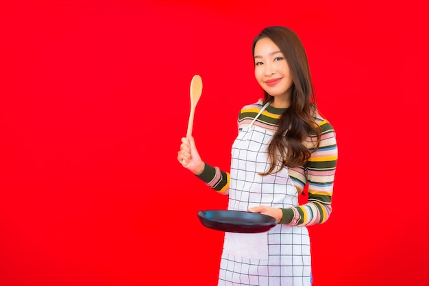 Ritratto bella giovane donna asiatica con padella pronta da cucinare sulla parete rossa