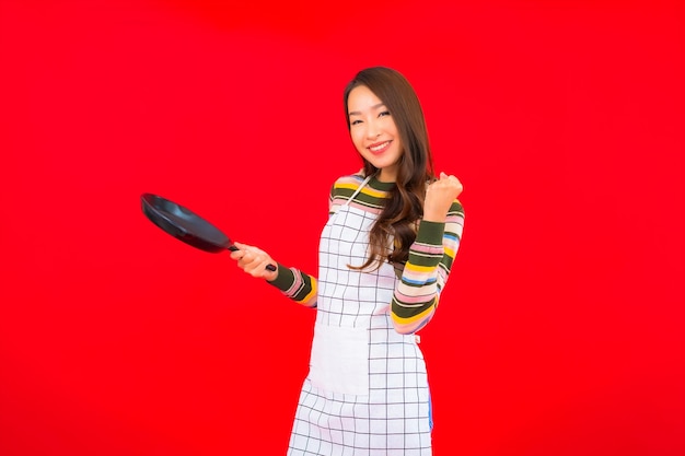 Portrait beautiful young asian woman with pan ready to cook on red wall