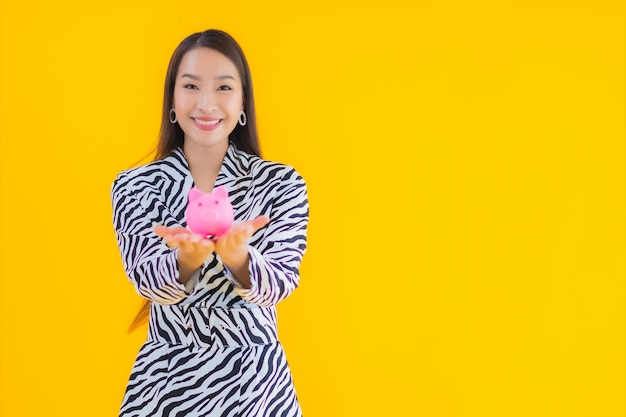 Portrait beautiful young asian woman with piggy bank and cash or money on yellow