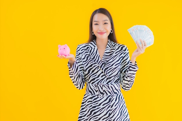 Portrait beautiful young asian woman with piggy bank and cash or money on yellow