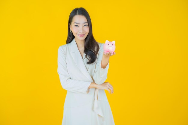 Portrait beautiful young asian woman with piggy bank on color background