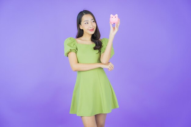 Portrait beautiful young asian woman with piggy bank on color background