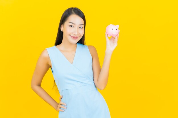 Portrait beautiful young asian woman with piggy bank on yellow color wall