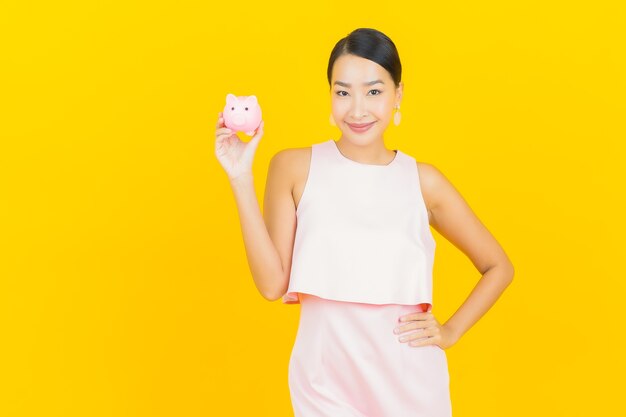 Portrait beautiful young asian woman with piggy bank on yellow