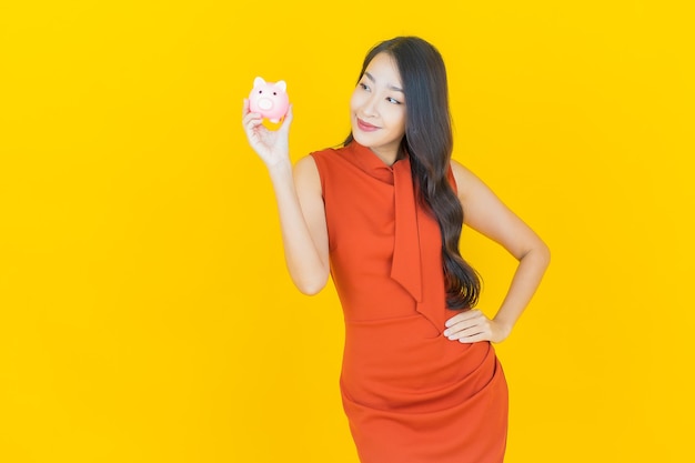 Portrait beautiful young asian woman with piggy bank on yellow