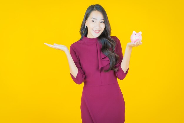 Portrait beautiful young asian woman with piggy bank on yellow