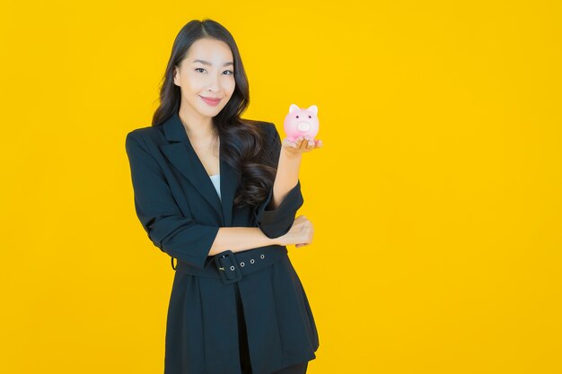 Portrait beautiful young asian woman with piggy bank on yellow