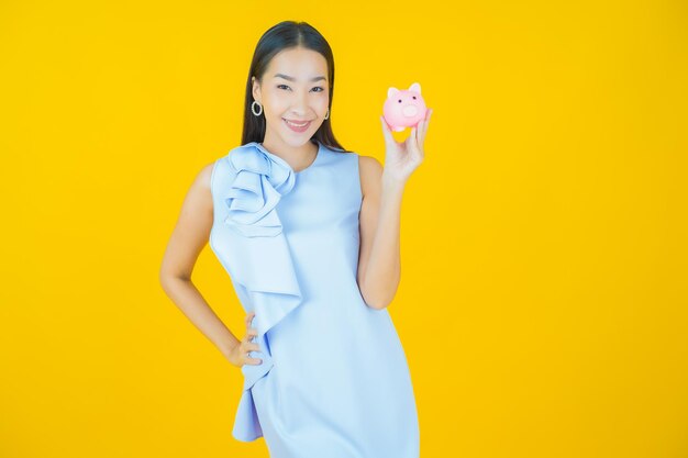 Portrait beautiful young asian woman with piggy bank on yellow