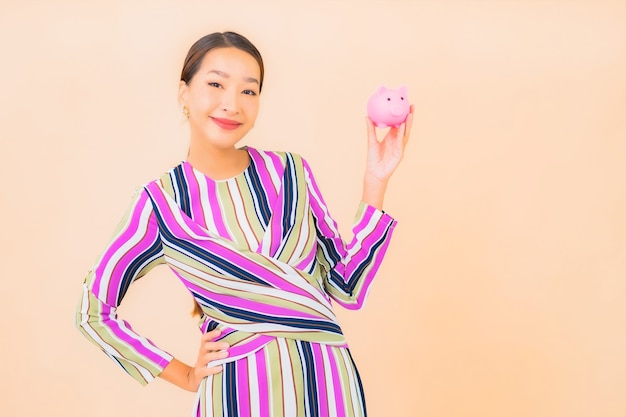 Portrait beautiful young asian woman with pink piggy bank on color