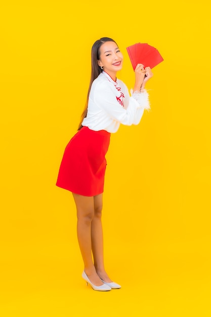 Портрет красивой молодой азиатской женщины с красным конвертом в китайском новом году на желтом
