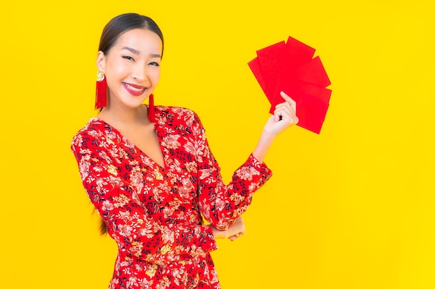 Foto gratuita bella giovane donna asiatica del ritratto con le buste rosse sulla parete gialla