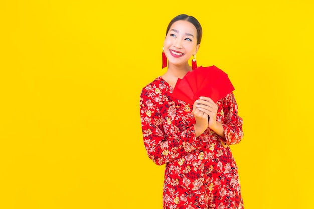 Bella giovane donna asiatica del ritratto con le buste rosse sulla parete gialla