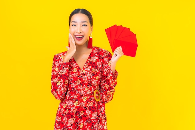 Portrait beautiful young asian woman with red envelopes on yellow wall