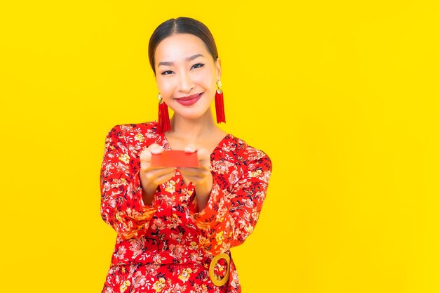 Женщина портрета красивая молодая азиатская с красными конвертами на желтой стене