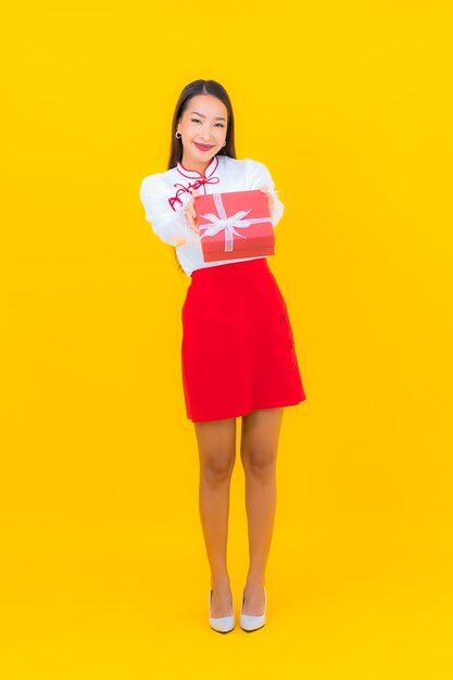 Женщина портрета красивая молодая азиатская с красной подарочной коробкой на желтом