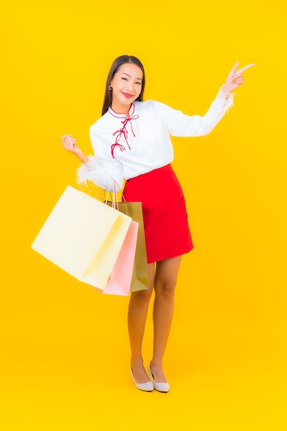 黄色のショッピング バッグとクレジット カードを持つ美しい若いアジア女性の肖像画