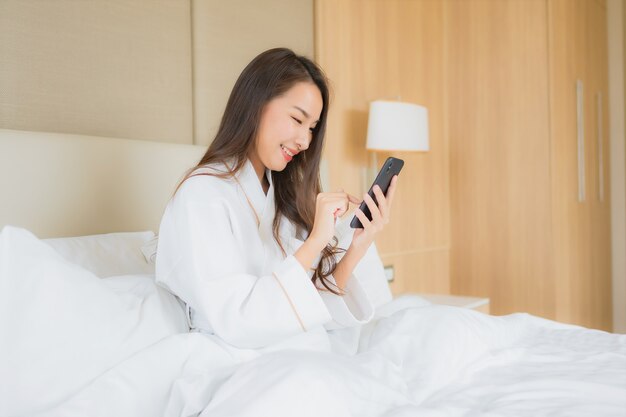 Женщина портрета красивая молодая азиатская с умным мобильным телефоном в спальне
