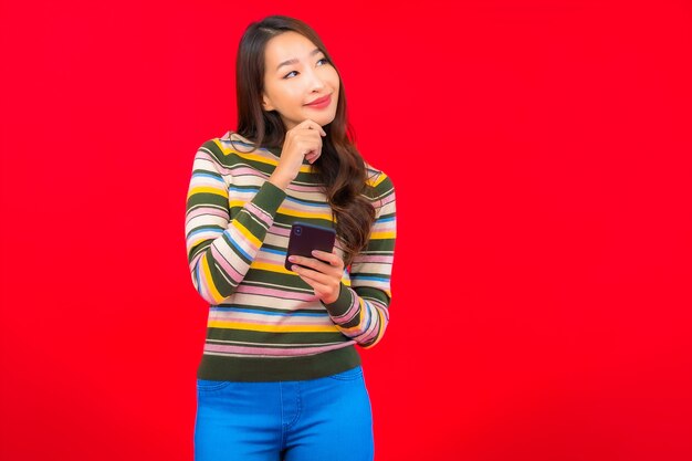 Женщина портрета красивая молодая азиатская с умным мобильным телефоном на красной стене